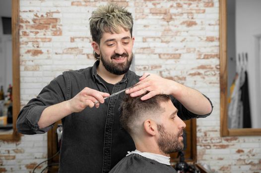 Barber cutting hair with scissors to a handsome young man . High quality photography