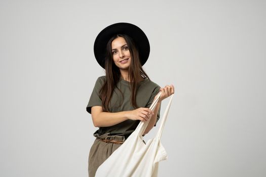 Happy smiling brunette woman in black hat with white cotton eco bag on her shoulder. Girl holding textile grocery bag with vegetables. Zero waste concept