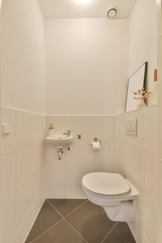 Modern toilet with a small sink in the corner lined with beige tiles