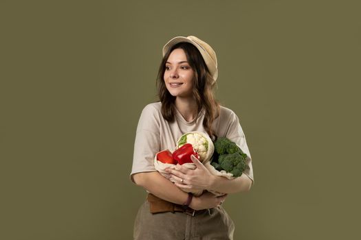 Zero waste concept. Young brunette woman holding reusable cotton shopping mesh bag with organic groceries from a market. Concept of no plastic. Zero waste, plastic free. Sustainable lifestyle