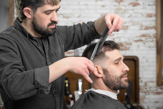 Barber cutting hair with scissors to a handsome young man . High quality photography