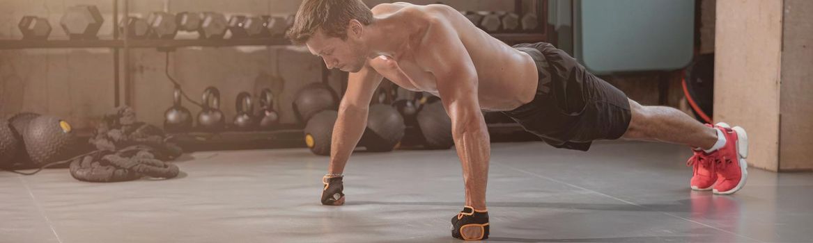 Strong muscular man standing in plank, looking down and actively training in the fitness club