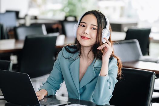 Asian female worker listening to music with smiling face to relieve stress while working at computer to rest her head and eyes