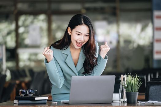 Business finance and investment, a business woman expresses happiness after successfully investing in the stock market on the Internet through a computer placed on a desk