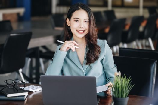 Asia woman entrepreneur or businesswoman showing a smiling face while reading a book developing financial and investing strategies and operating a computer tablet working on a wooden table