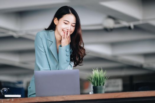 Business finance and investment, a business woman expresses happiness after successfully investing in the stock market on the Internet through a computer placed on a desk