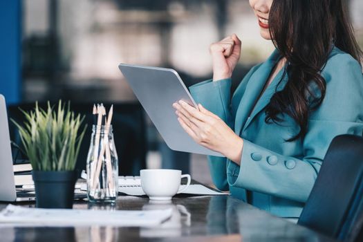 Business finance and investment, a business woman expresses happiness after successfully investing in the stock market on the Internet through a tablet placed on a desk