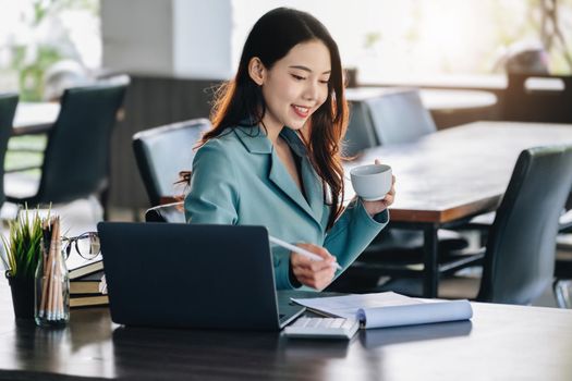 Young economist or accountant or financier and investor is drinking coffee while reading budget documents and use computers to study the impact and risk assessment of corporate investment management