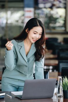 Business finance and investment, a business woman expresses happiness after successfully investing in the stock market on the Internet through a computer placed on a desk