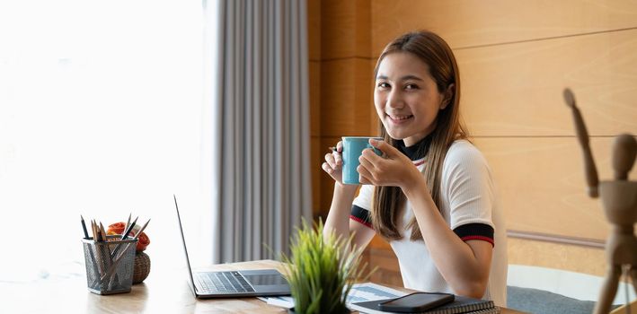 Portrait of smiling beautiful asian woman relaxing using technology of laptop computer while sitting on table.Young creative girl working and typing on keyboard at home.work at home concept.