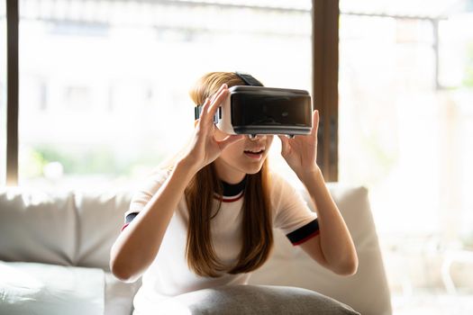 Excite asian woman playing online game with vr glasses and controller at her home.