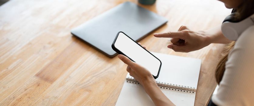 Top view Woman sitting and holding blank screen mock up mobile phone on wooden desk,