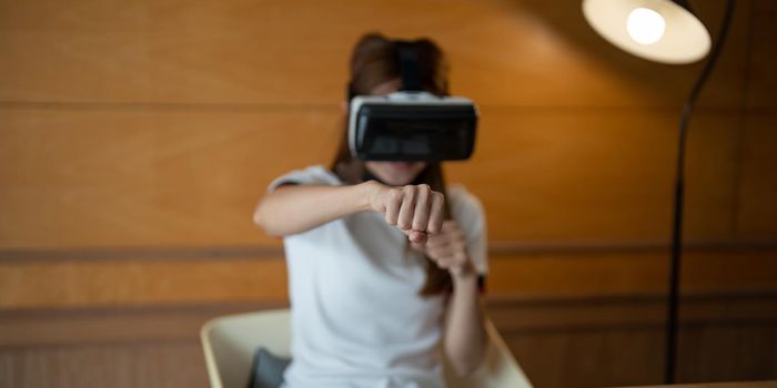 Girl wearing virtual reality glasses on head playing fighting game, holding clenched fists up ready to boxing, experiencing cyberspace using VR headset technology.