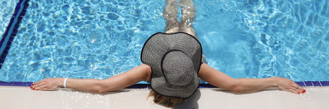 Top view of woman in luxury five stars spa resort in swimming pool, unrecognizable woman in big hat relaxing in clean water. Summer holiday, chill, relax, traveling concept