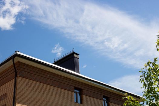 A roof with a chimney on the background of a blue summer sky