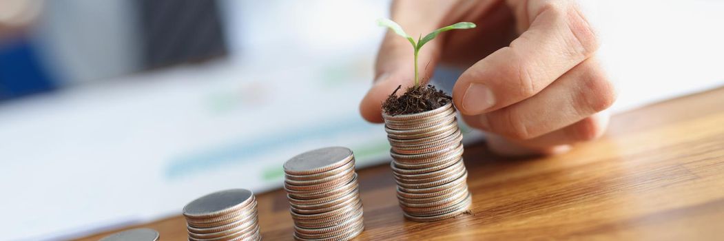 Close-up of male hand putting coin with plant on pile. Upward money growth, diagram statistics, price and salary growth, progress. Financial growing and economy improvement