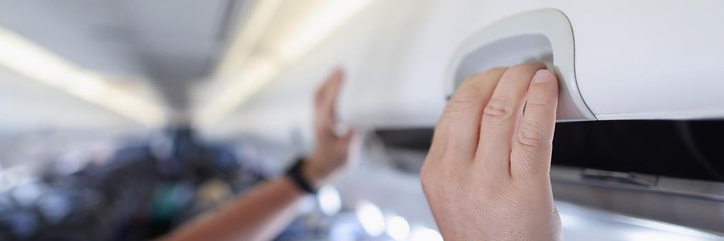 Close-up of man open or close carry-on luggage rack in airplane, put suitcase in overhead shelf in airplane cabin. Comfort for passenger during flight. Takeoff, landing concept