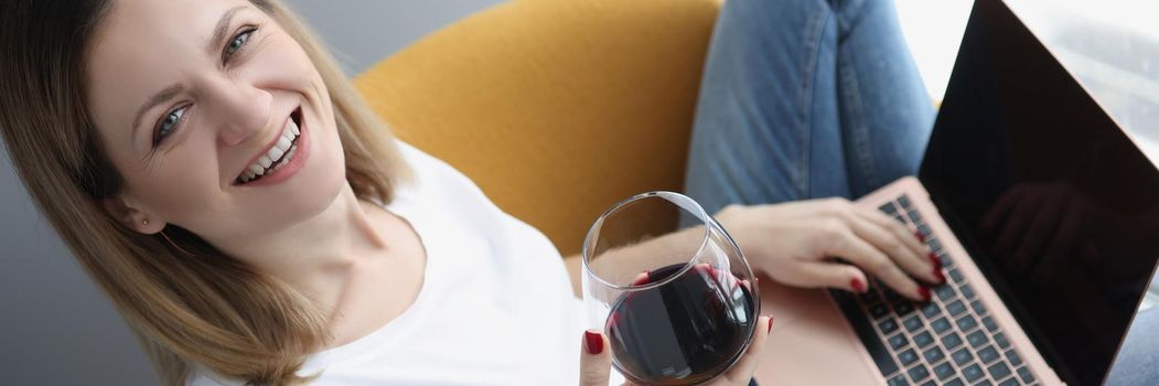 Top view of happy woman drink wine and work on laptop, start day with glass of wine. Freelancer girl work from home in chair. Remote job, freelance, break from work concept