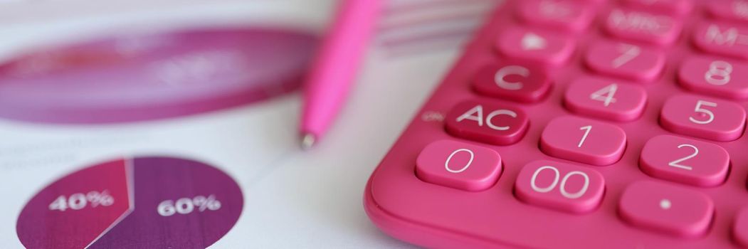 Close-up of paper with graphs and diagrams, pink calculator and pink pen, female workplace. Tools to analyze profit. Accounting, business, banking, financial and tax system concept