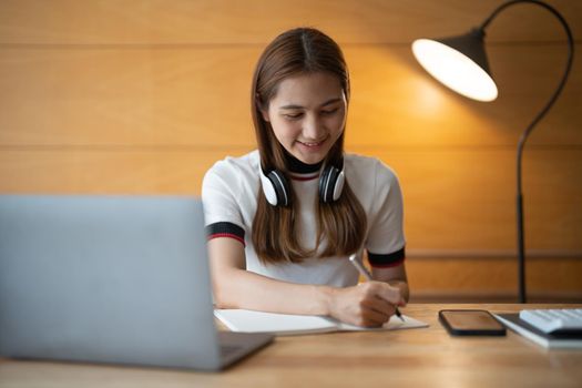 Asian woman writing making list taking notes in notepad working or learning on laptop indoors- educational course or training, seminar, education online concept.