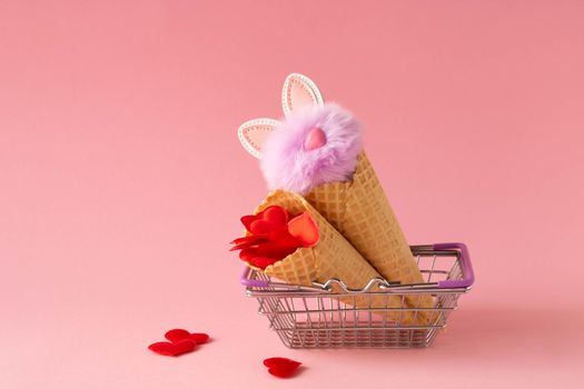 Abstract pink background with red hearts and a fluffy lilac rabbit in a grocery basket and waffle cones. The concept of love, a greeting card for Valentine's Day and Easter.