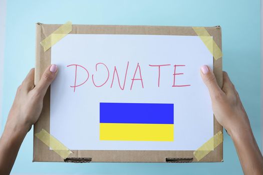 Top view of person holding ukraine donation box for help, donate food, clothes, money for other people wellbeing. Put container in public place. Donation, give, sacrifice concept