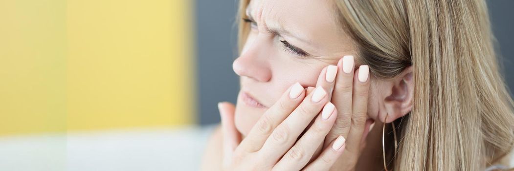 Portrait of beautiful young woman suffering from tooth pain, hold hand near cheek, feeling unwell because of tooth decay or sensitivity. Dental problem, healthcare, toothache concept