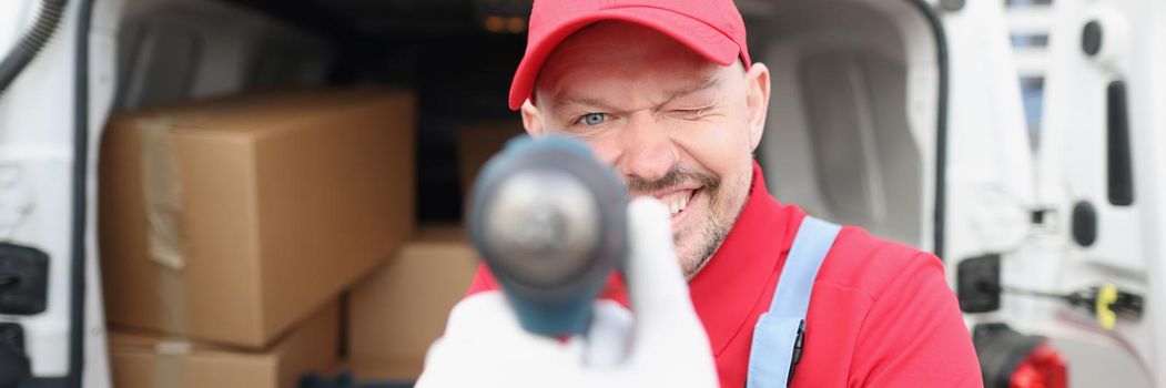 Portrait of cheerful courier man having fun during delivery, pretending hes shooting from gun, making jokes at work. Delivery service, shipment, spread joy and happiness concept