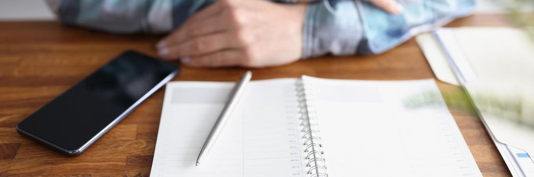 Close-up of open planner on wooden table, person with folded arms. Need to start planning week, meetings, write down thoughts and ideas. Personal diary, creative, journaling concept. Copy space