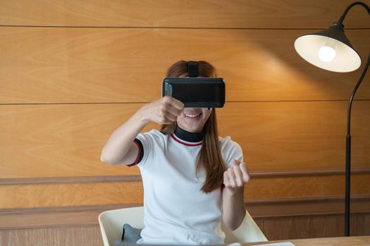 Excited young woman in VR goggles driving car in virtual reality. Lady screaming when turning virtual steering wheel, teen playing in racing computer game or road simulator,