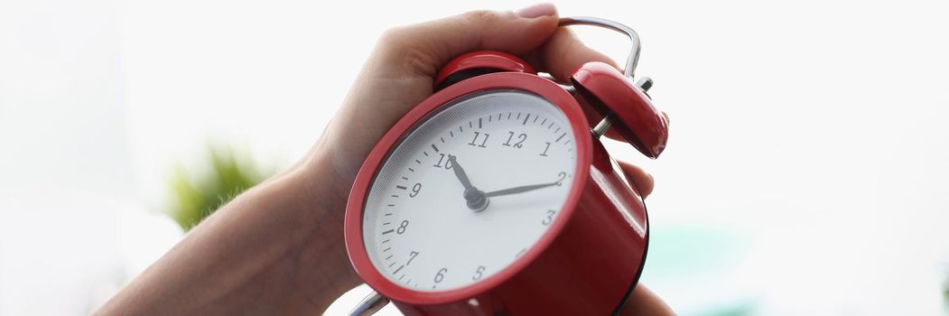 Close-up of woman setting red vintage alarm on proper time, spin arrows on dial, black numbers. Prepare alarm on morning, wake up for work, timer, timepiece concept