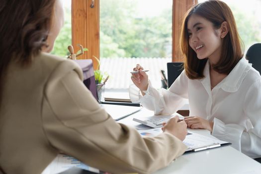 Two young beautiful asian business woman in the conversation, exchanging ideas at modern office