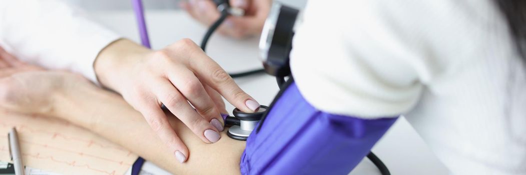 Close-up of female therapist hands holding tonometer and checking blood pressure of woman patient. Medical examination, treatment and medicine concept