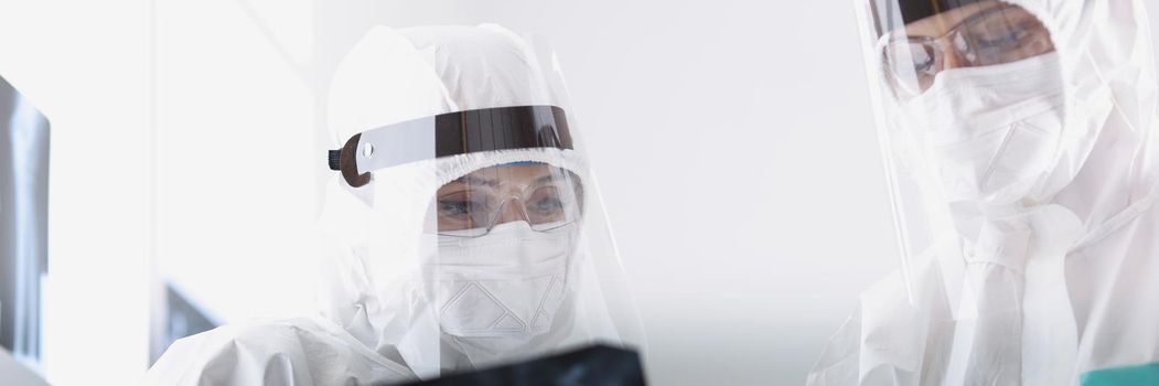 Close-up of therapists in protective medical suits looking carefully at radiograph of sick patient. Coronavirus outbreak and worldwide pandemic concept