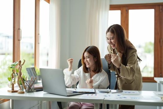 Happy young business asian team looking at laptop screen, celebrating success, Raising arms in a celebration of a successful