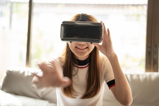 Excite asian woman playing online game with vr glasses and controller at her home.