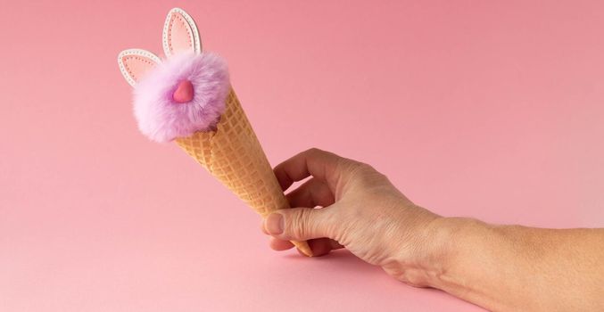 Abstract pink background. A hand with a fluffy lilac rabbit in a waffle cone. The concept of love, a greeting card for Valentine's Day and Easter.