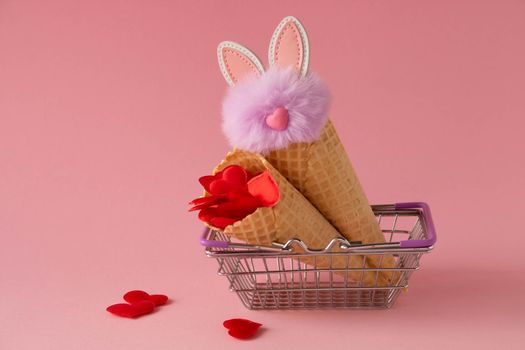 Abstract pink background with red hearts and a fluffy lilac rabbit in a grocery basket and waffle cones. The concept of love, a greeting card for Valentine's Day and Easter