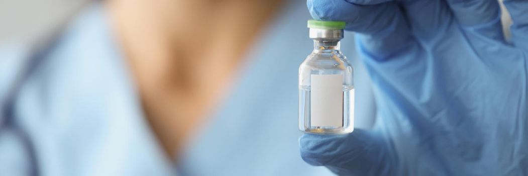Close-up of doctor hand holding glass bottle with vaccine. Medical ampoule with transparent substance against virus. Vaccination, immunization and coronavirus outbreak concept