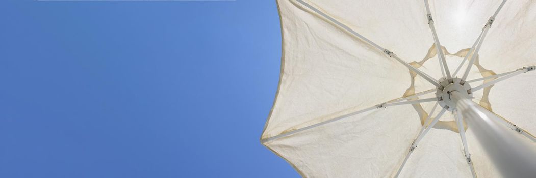 Close-up of white beach parasol, metal stalk and round shaped cover to create shadow from sun. Piece of blue summer sky. Summertime, tourism, holiday, beach equipment concept