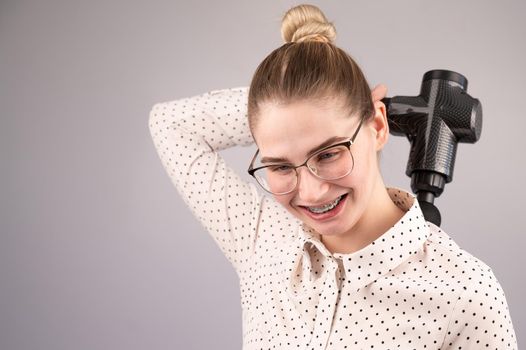 Smiling woman with braces uses a massager gun for her back