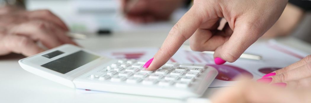 Close-up of woman with pink nails calculate profit, press on number knobs. Mess on working desk, work in process, solve financial problems. Business, economy, banking concept