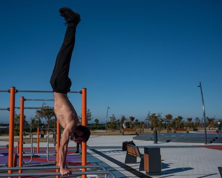 Shirtless man doing handstand on parallel bars at sports ground