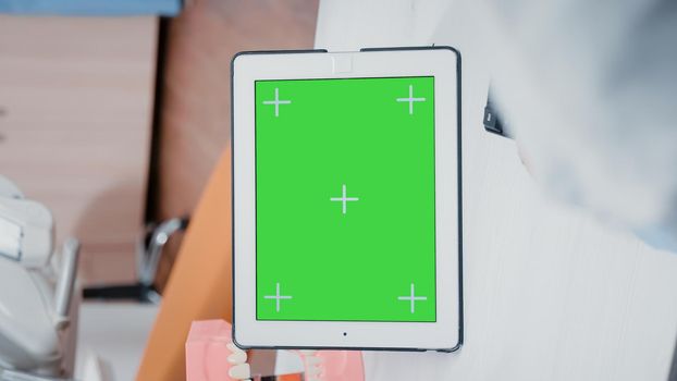 Vertical video: Close up of dentist using green screen on tablet for teethcare in stomatology office. Orthodontist working with chroma key and isolated mockup template on device for oral care