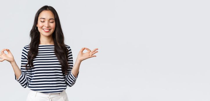 Lifestyle, people emotions and casual concept. Calm happy young woman feeling peaceful during meditation, close eyes and smiling as hold hands in zen nirvana gesture, do yoga exercise.