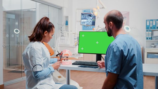Man and woman working with green screen and teeth layout for oral care at dental cabinet. Dentist and assistant using chroma key and isolated background on computer for teethcare.