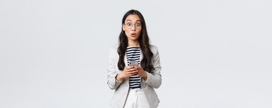 Business, finance and employment, female successful entrepreneurs concept. Surprised asian businesswoman in glasses and suit react astonished, holding mobile phone.