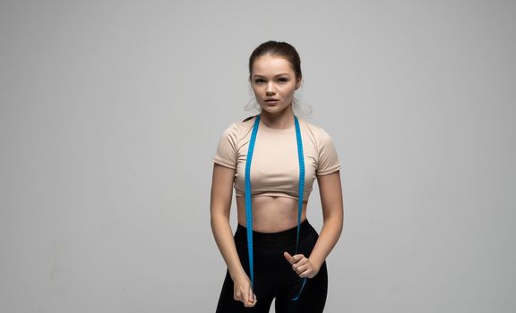 Sport fitness attractive young brunette girl in sportswear with blue measuring tape on her shoulder on white background Sports and diets