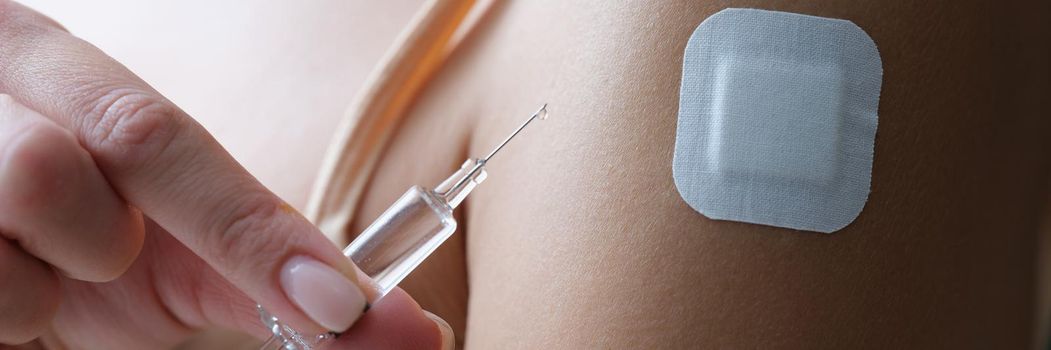 Close-up of female shoulder with patch. Woman holding injection syringe with transparent liquor. Vaccination, immunization against coronavirus and treatment concept