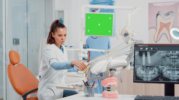 Woman using horizontal green screen on monitor in dental cabinet while man assistant giving teeth radiography for examination. Dentist working with mockup template and chroma key